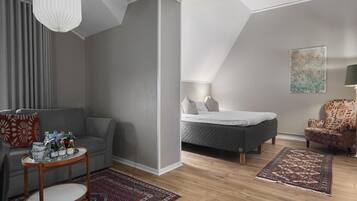 Una sala de estar moderna con un sofá gris, una mesa de centro redonda de madera, un tapete estampado, una cama con edredón gris y una silla con estampado floral.