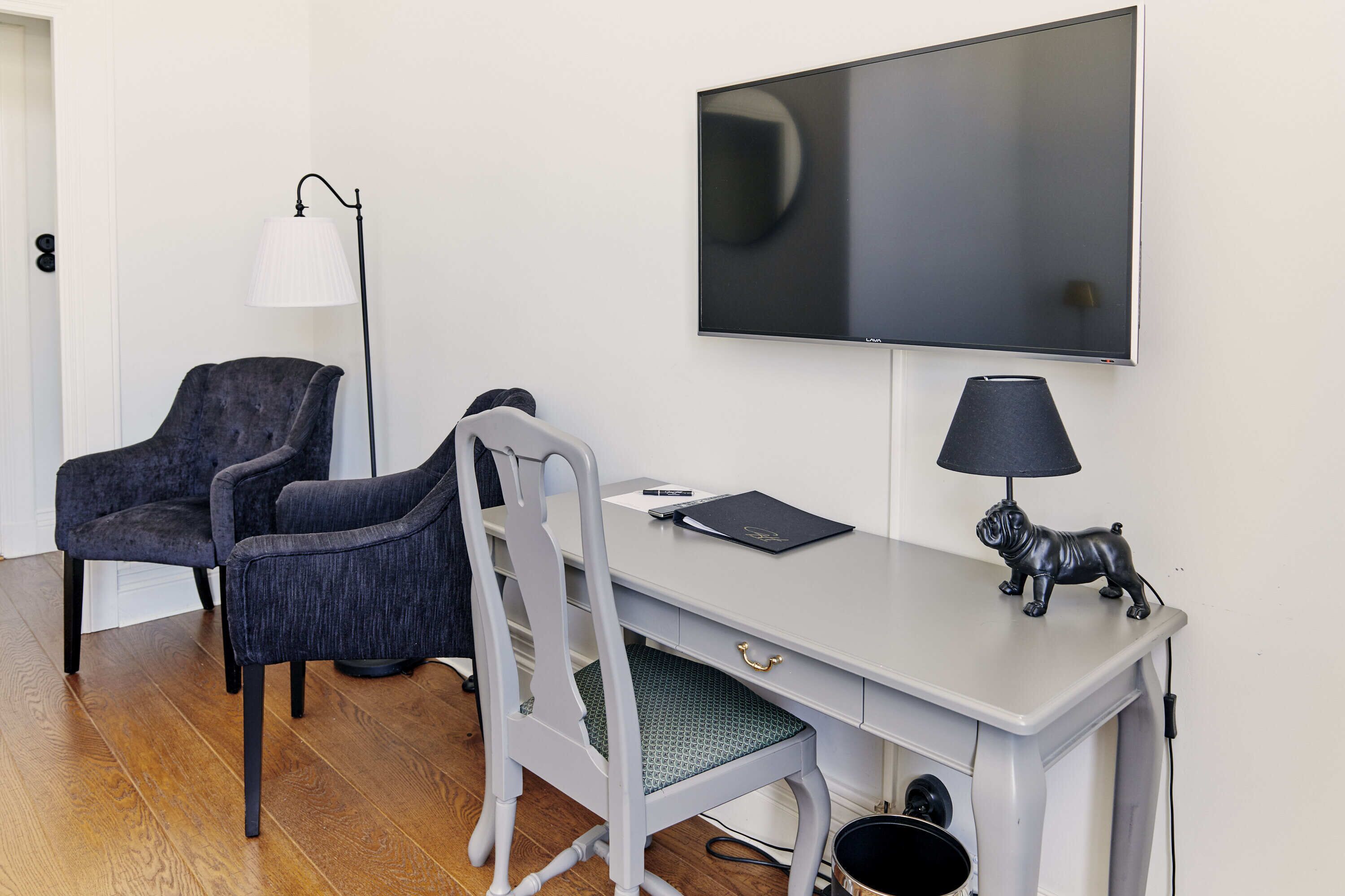 A room with a desk, two chairs, a television, a lamp, and a small figurine.