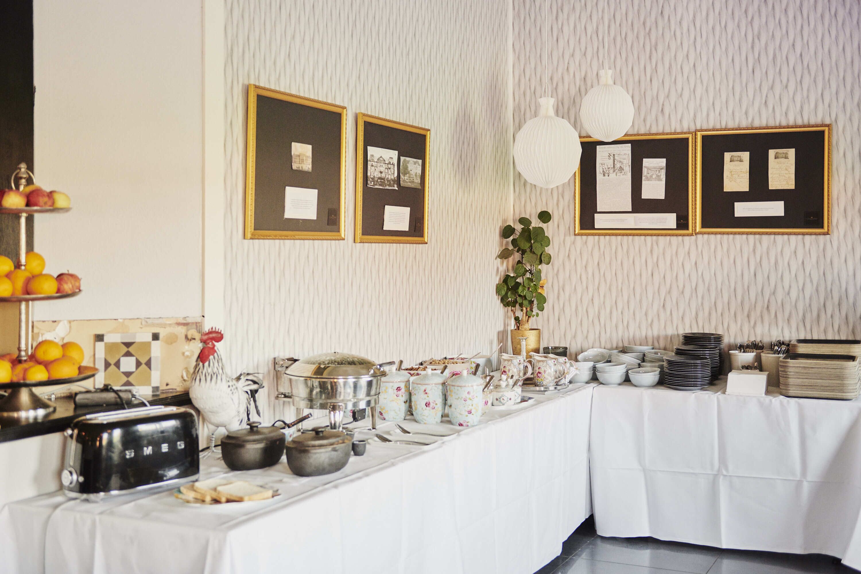 A buffet setup with a variety of dishes, a vintage toaster, and framed pictures on the wall.