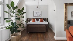 Un dormitorio con una cama, una planta grande en maceta, una lámpara colgante y un cuadro en la pared.