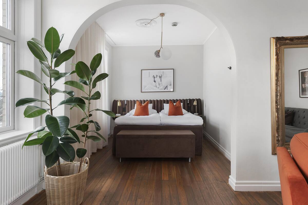 A bedroom with a bed, a large potted plant, a hanging light fixture, and a framed picture on the wall.
