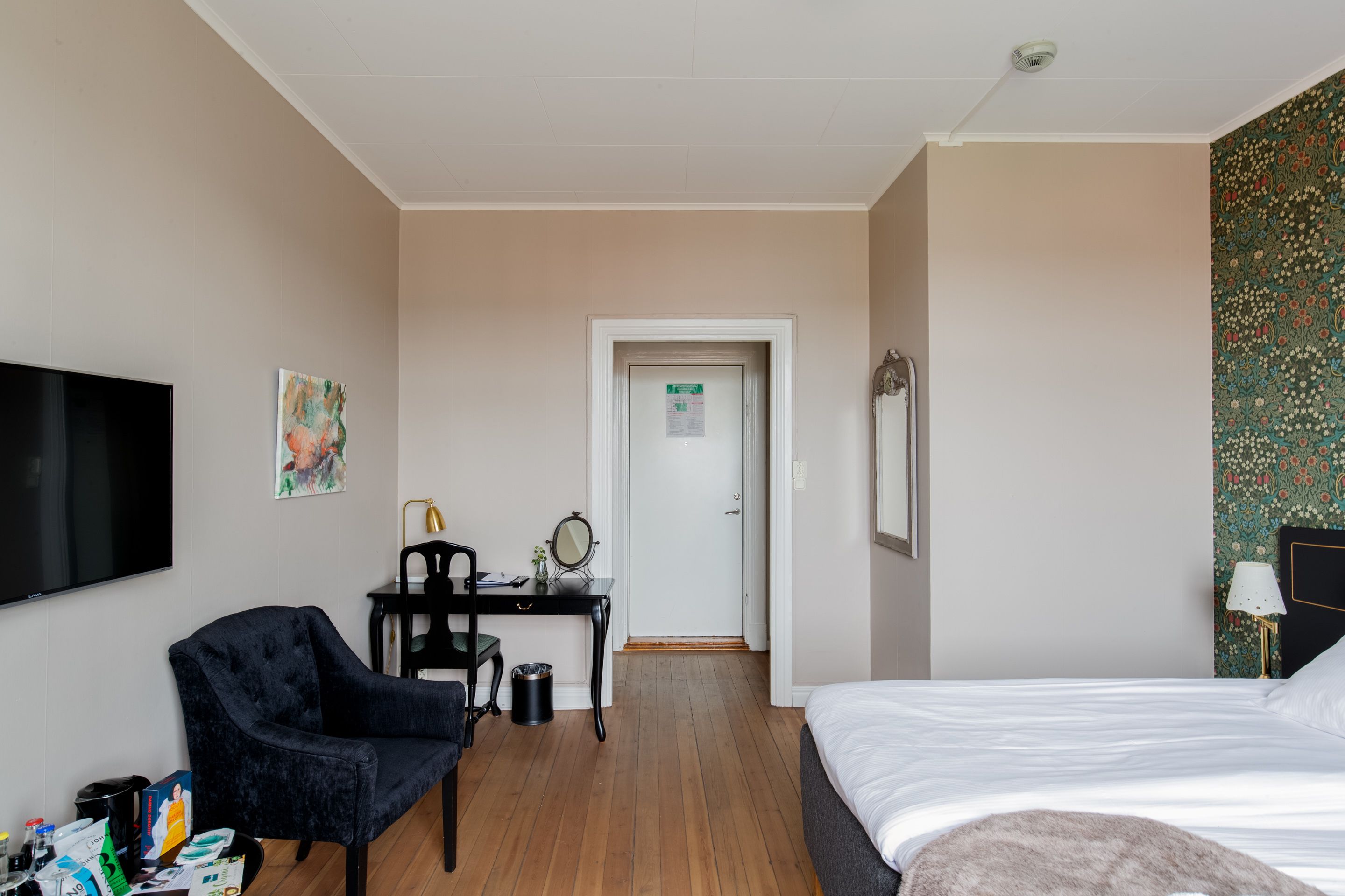 A hotel room with a bed, a desk with a chair, a television, and a door leading to another room.