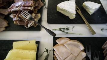 Variedad de quesos y embutidos sobre una mesa con tenedores y un cuchillo.