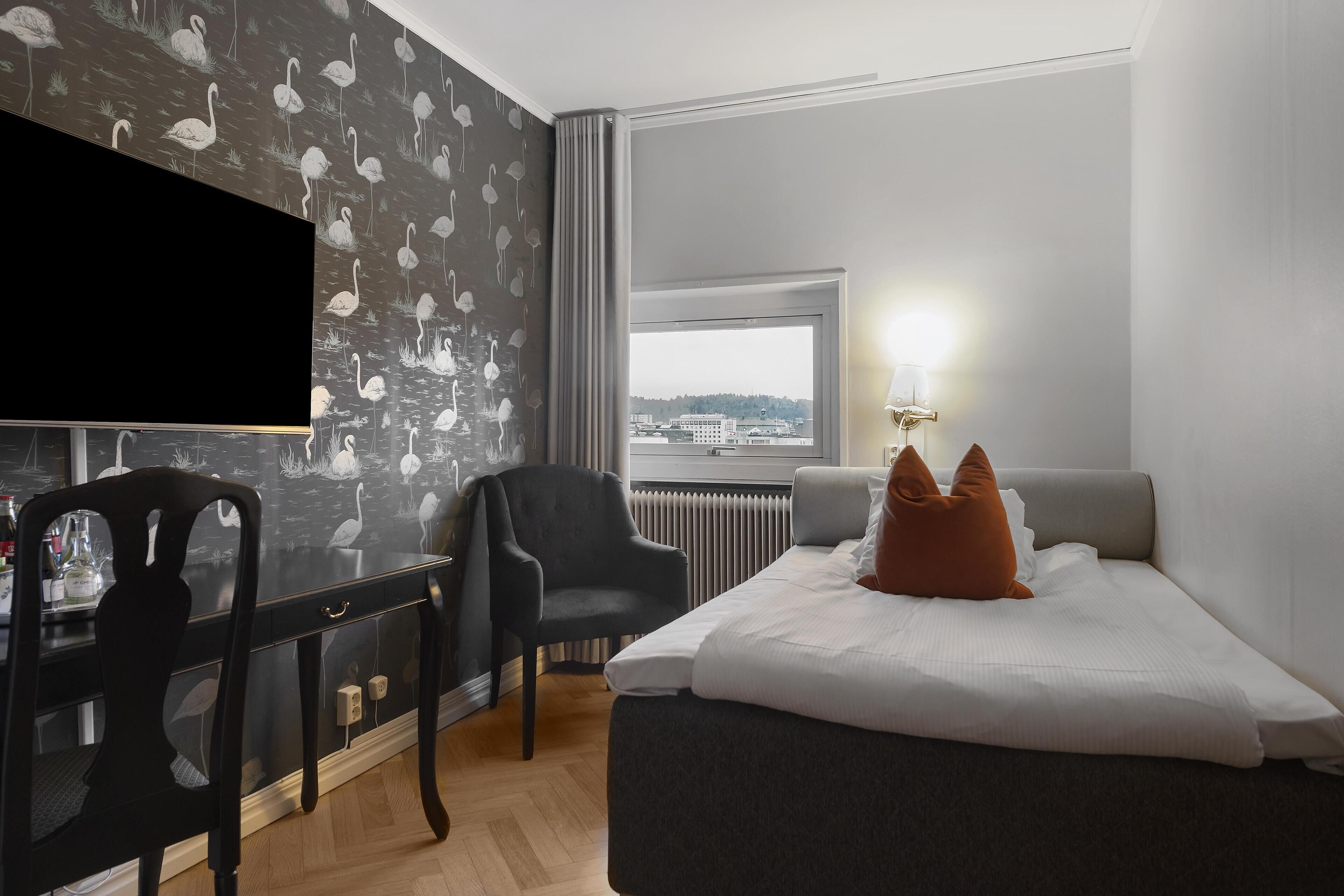 Habitación de hotel con cama, escritorio, silla, televisión y ventana con vistas.