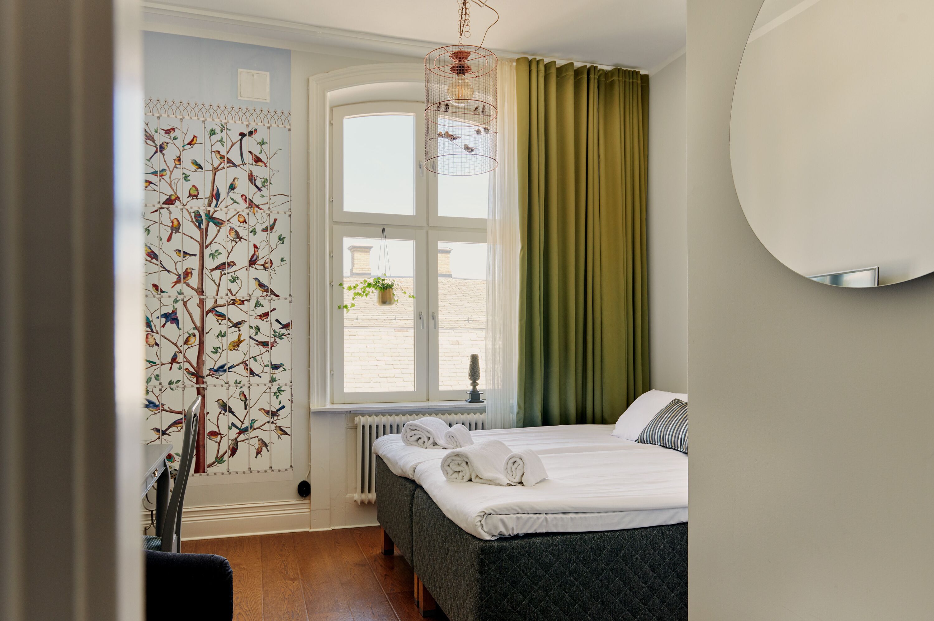 A bedroom with a bed, a window with curtains, a radiator, and a wall-mounted mirror.