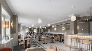 Un amplio vestíbulo de hotel con varias zonas de estar, un bar central y una cocina visible al fondo.