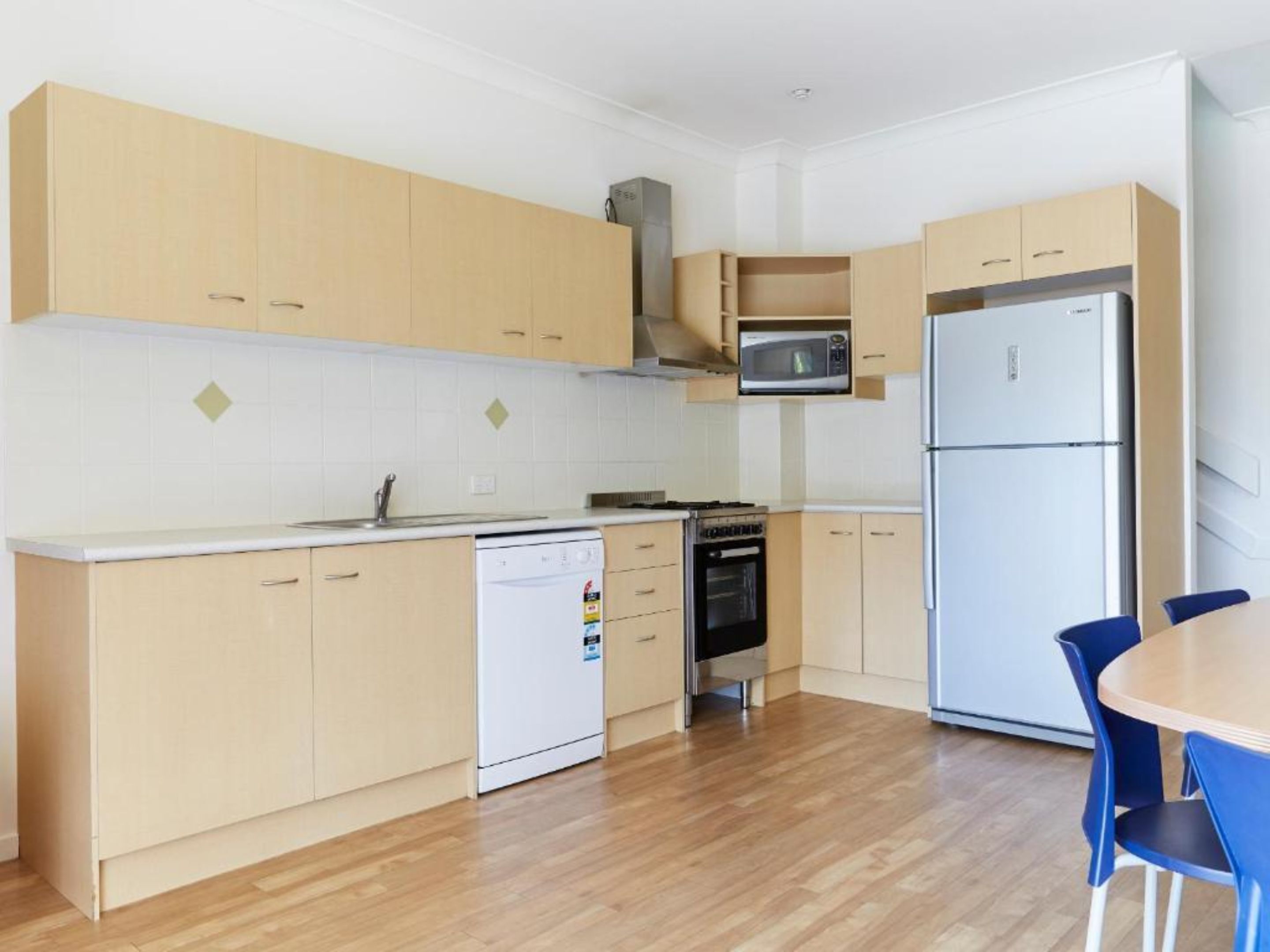 Une cuisine moderne avec des meubles en bois, un four à micro-ondes, un réfrigérateur, un lave-vaisselle et un coin repas avec des chaises bleues.