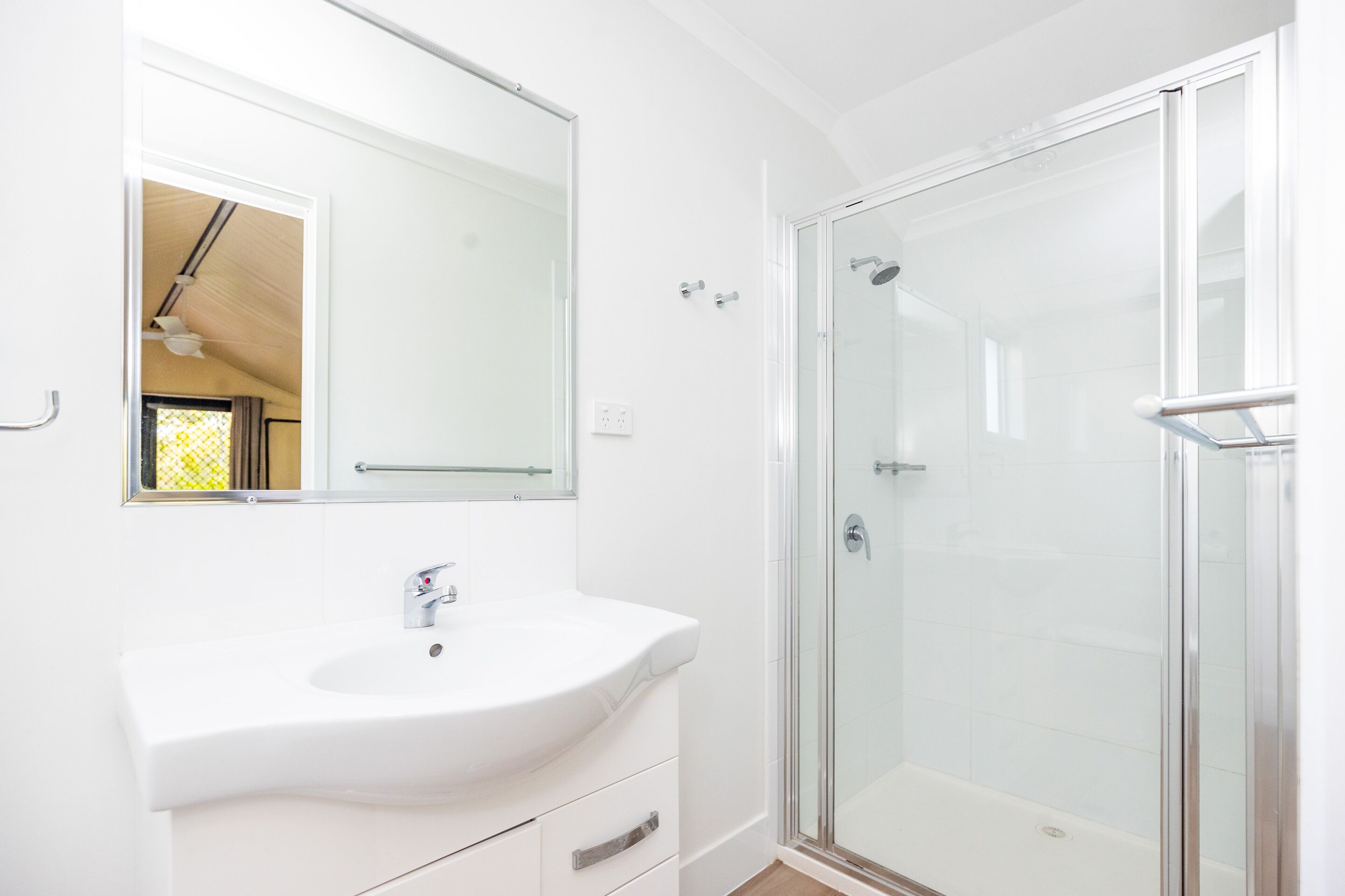 Un baño moderno con un lavamanos blanco, un espejo grande y una ducha con cerramiento de vidrio.