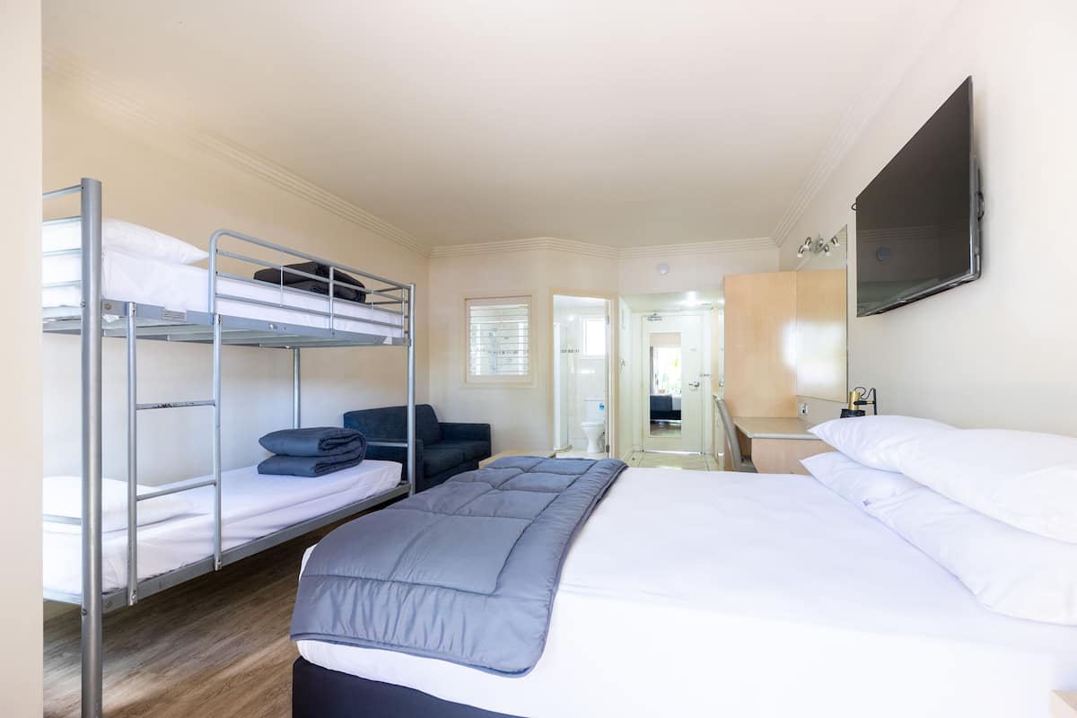 Une chambre d’hôtel avec des lits superposés, un lit simple, un téléviseur à écran plat, un bureau et un miroir.