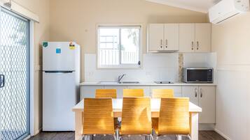 A compact kitchen with a refrigerator, microwave, and white cabinets. There is a dining table with chairs and a window with a view.