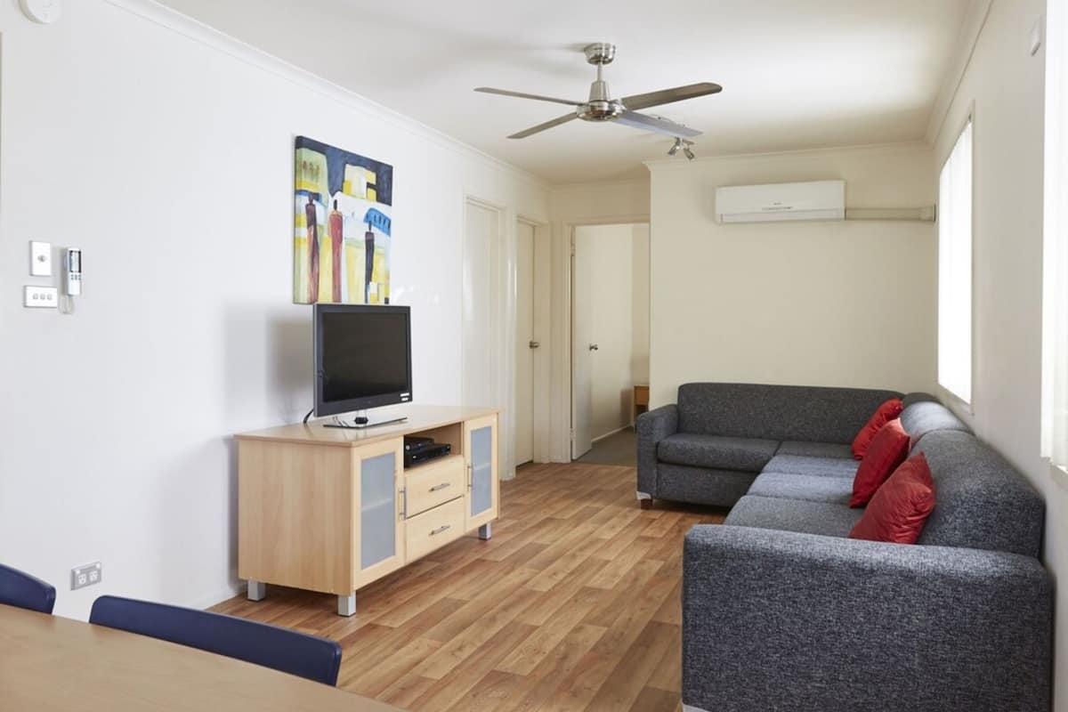 Un salon moderne avec un canapé gris, un meuble en bois sur lequel est posée une télévision et un ventilateur de plafond.