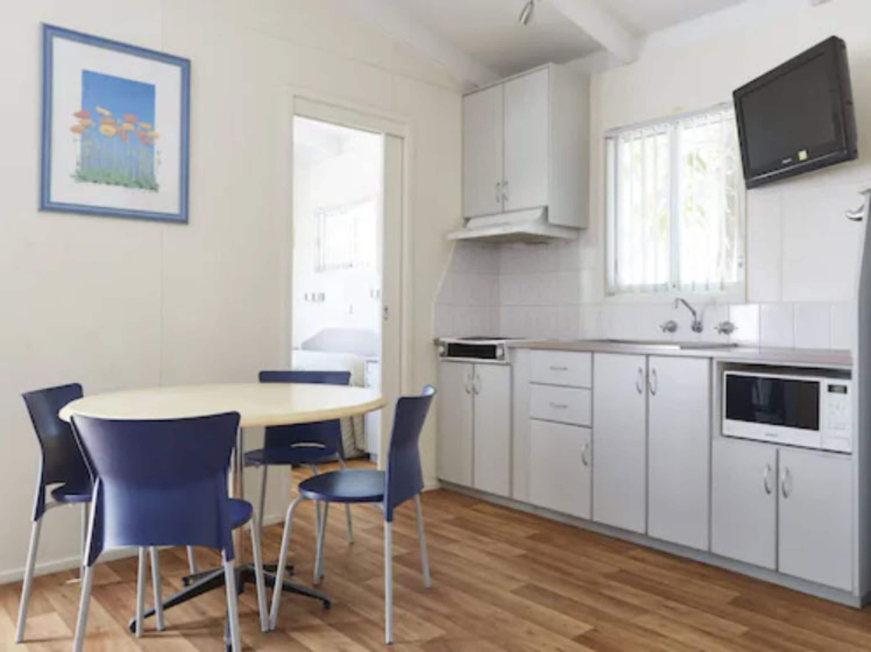 A compact kitchen with white cabinets, a microwave, and a TV mounted above the counter.