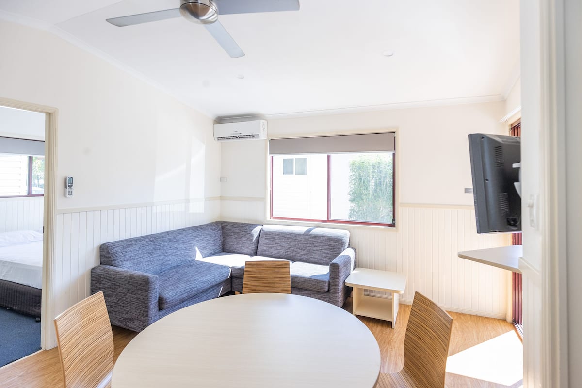 Une pièce moderne avec un canapé d’angle gris, une table ronde et un ventilateur de plafond.