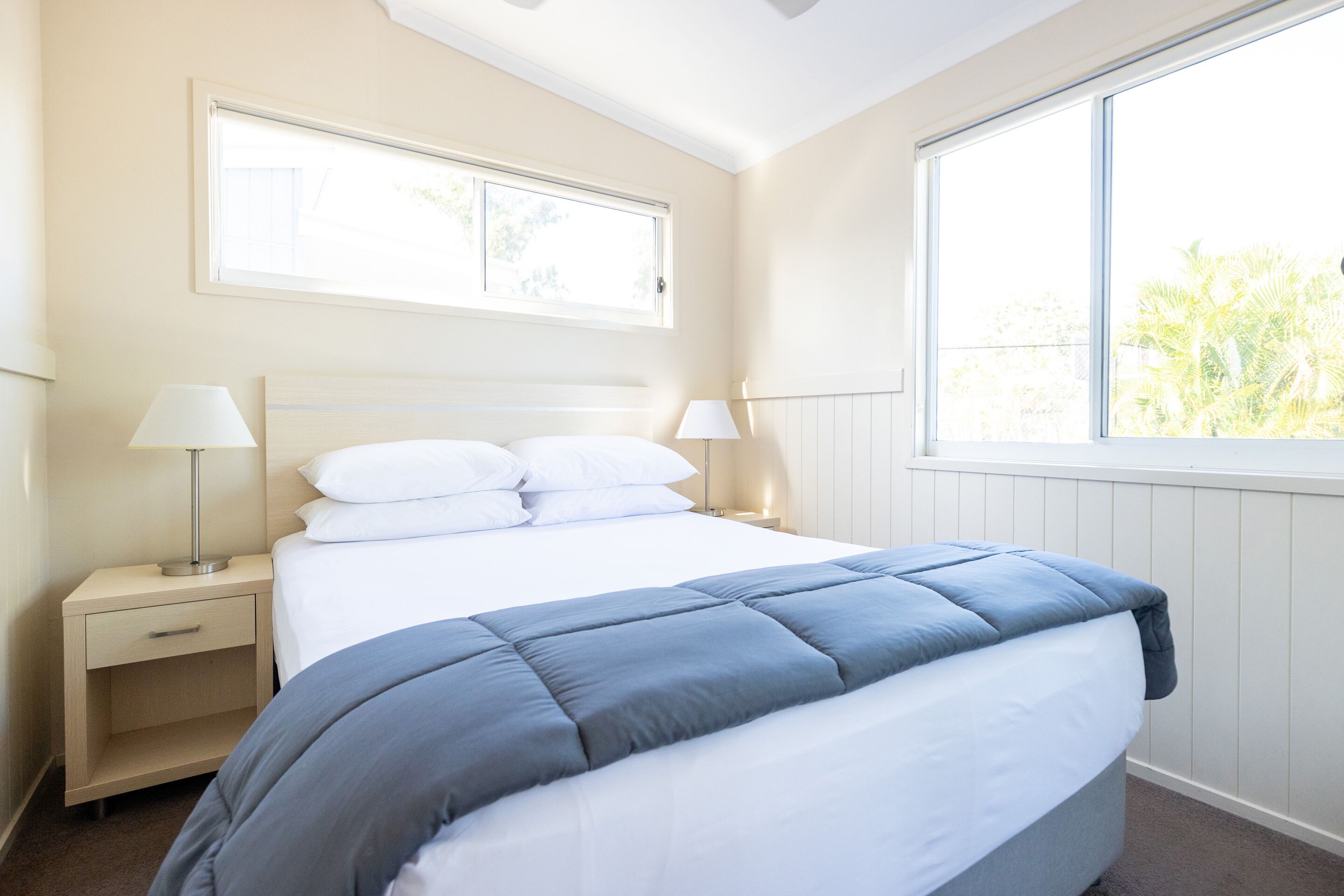 Un dormitorio ordenado con cama, mesitas de noche y ventana que ofrece vistas a zonas verdes.