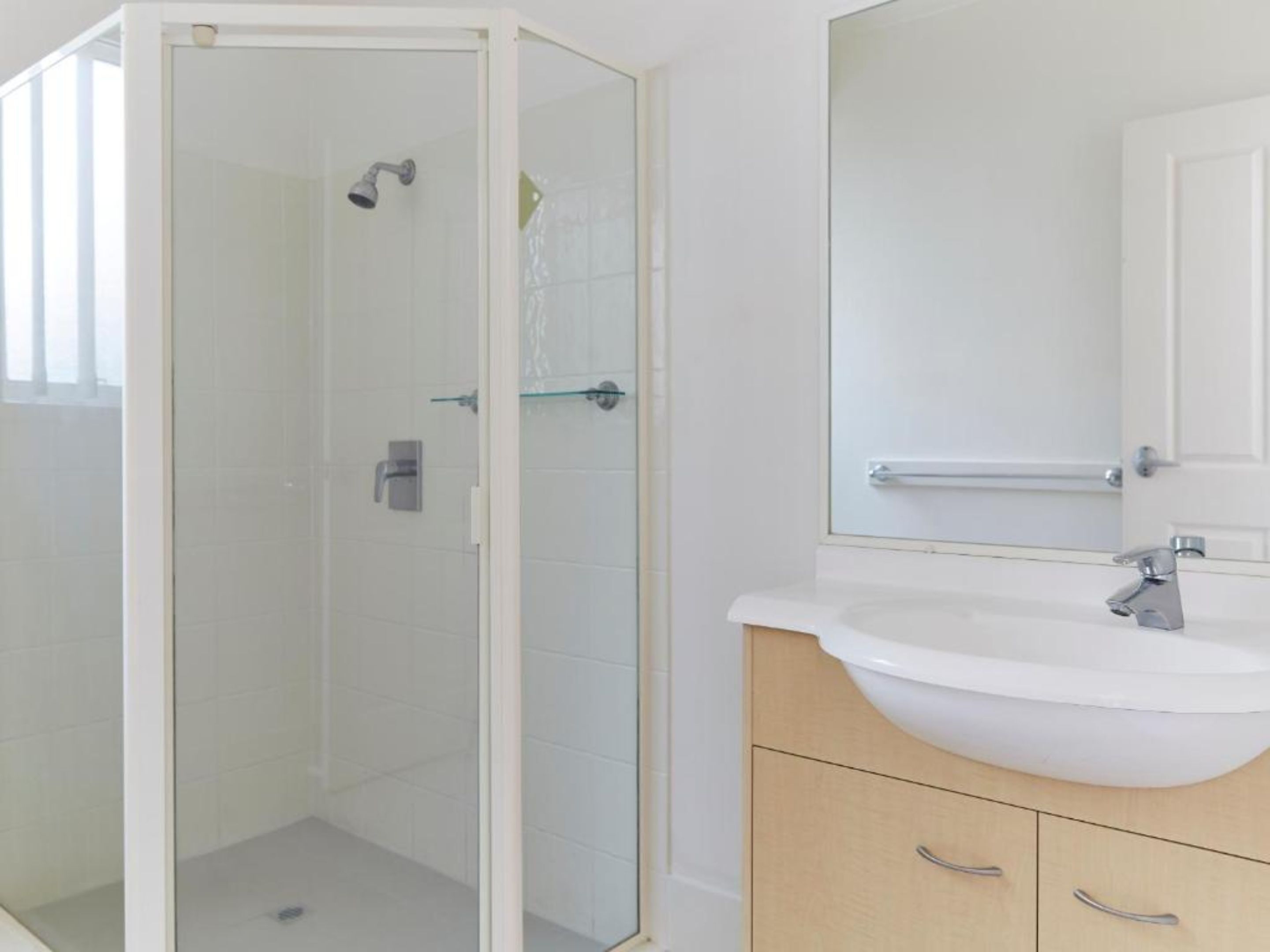 Un baño moderno con ducha de vidrio, lavamanos blanco y tocador de madera con cajones.