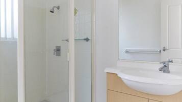 Un baño moderno con ducha de vidrio, lavamanos blanco y tocador de madera con cajones.