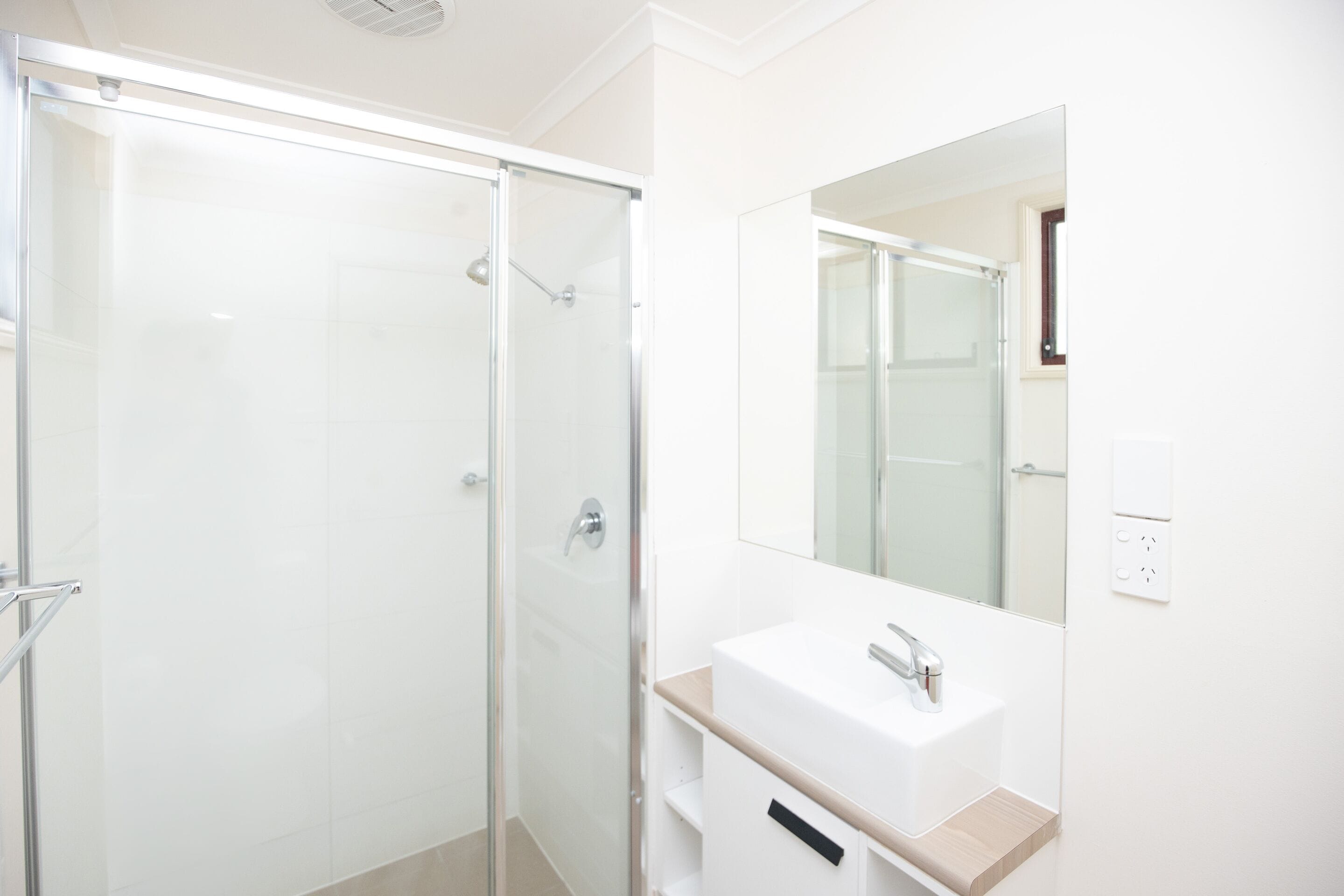 Une salle de bain moderne avec une douche à parois de verre, un lavabo blanc et un grand miroir.