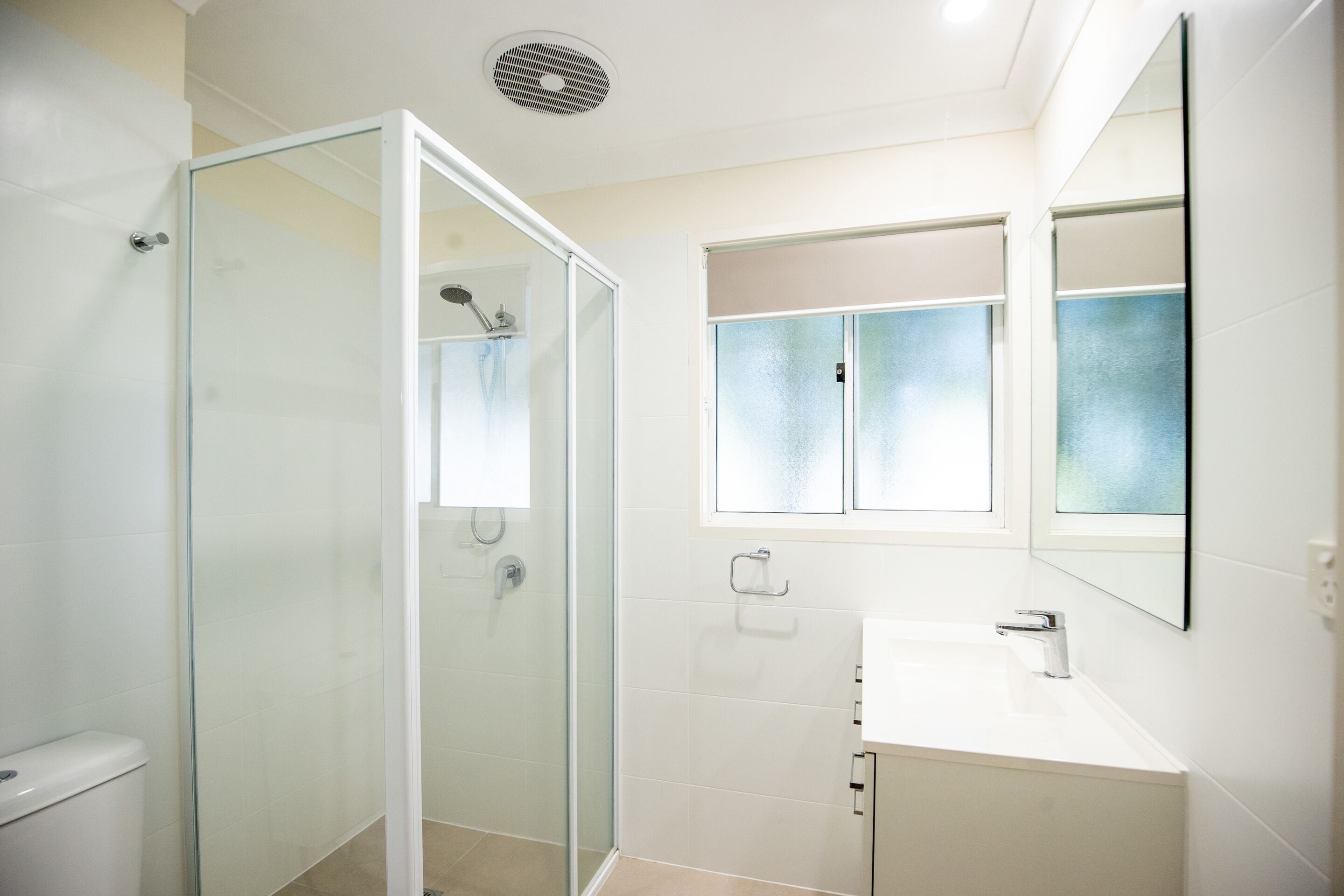 Un baño moderno con ducha envuelta en vidrio, un lavabo blanco y un espejo sobre él.