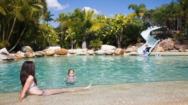 Zona de piscina con agua cristalina, un niño jugando y una mujer relajándose en el borde.