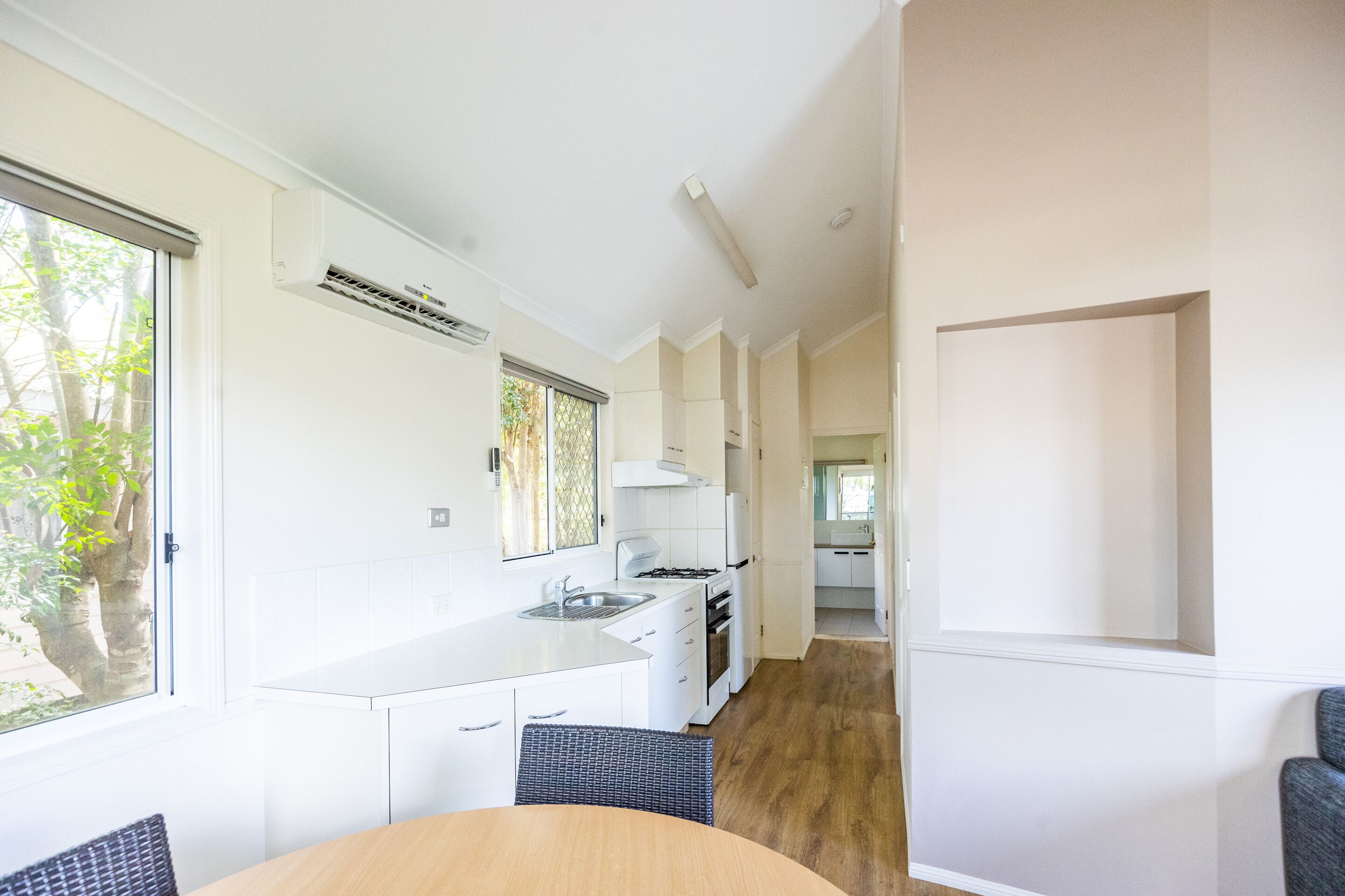 A modern kitchen with white cabinetry, a built-in stove, and a window with a view of trees.