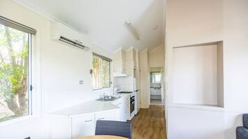 A modern kitchen with white cabinetry, a built-in stove, and a window with a view of trees.