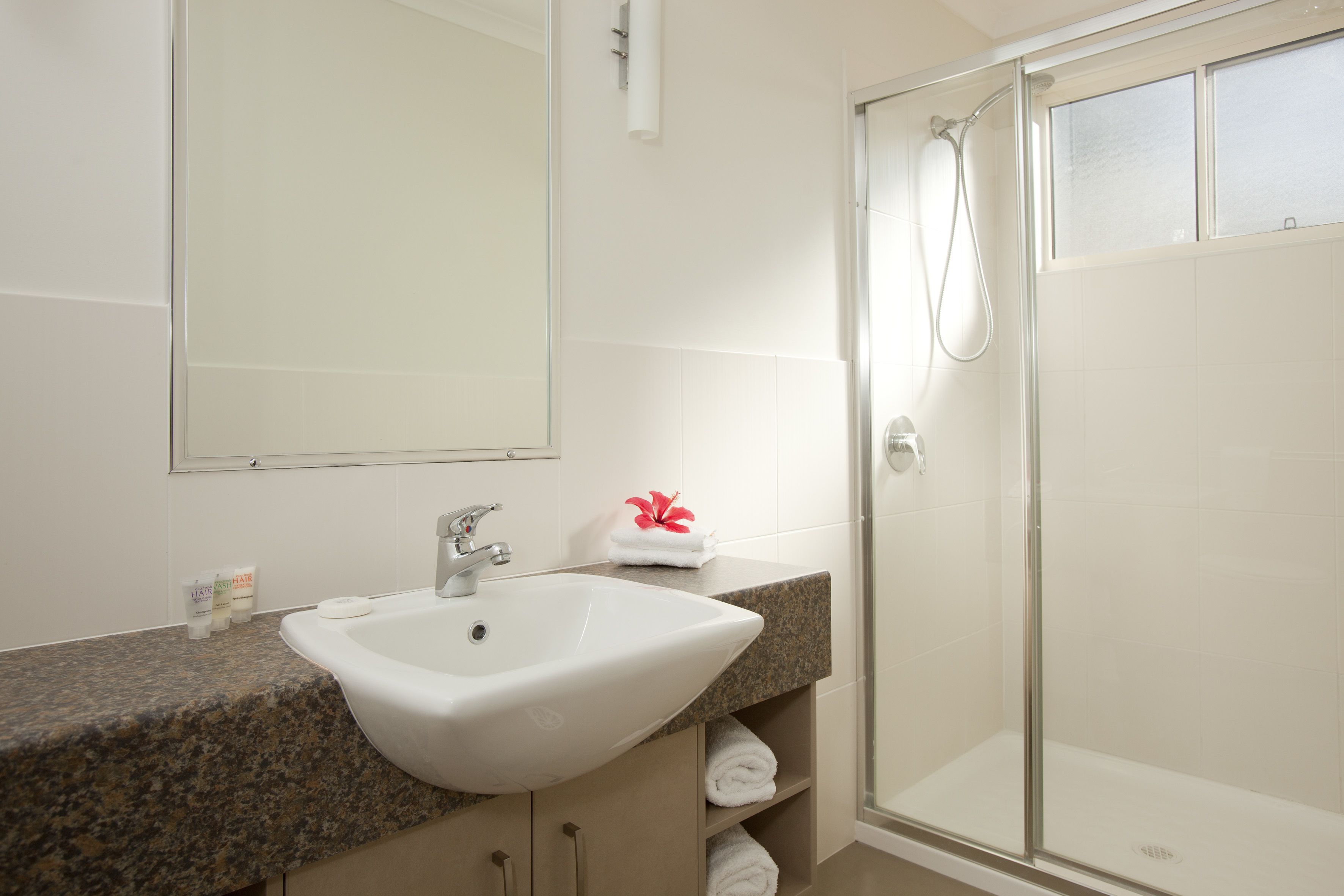 A bathroom with a granite countertop, a white sink, a mirror, a glass shower enclosure, and neatly folded towels.