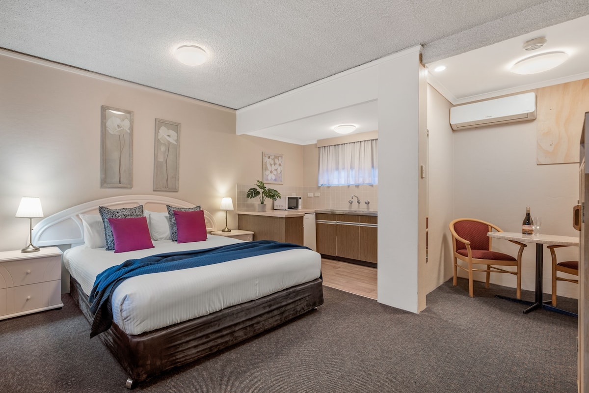 Ein Hotelzimmer mit Bett, Nachttischen, Schreibtisch, Stuhl, einer Mikrowelle, einem Waschbecken und einem Fenster mit Vorhängen.