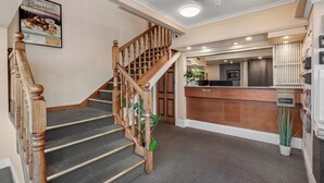 Un hall d’hôtel avec un escalier en bois, un comptoir d’accueil et une boîte pour déposer les clés.