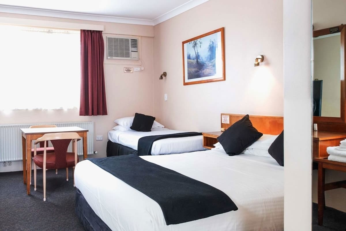 Ein Hotelzimmer mit zwei Betten, einem Schreibtisch, einem Stuhl, einem Heizkörper, einer Klimaanlage, einem Bild an der Wand und einem Spiegel.