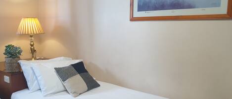 Una cama bien hecha con sábanas blancas y dos almohadas, una lámpara de noche y un cuadro en la pared.