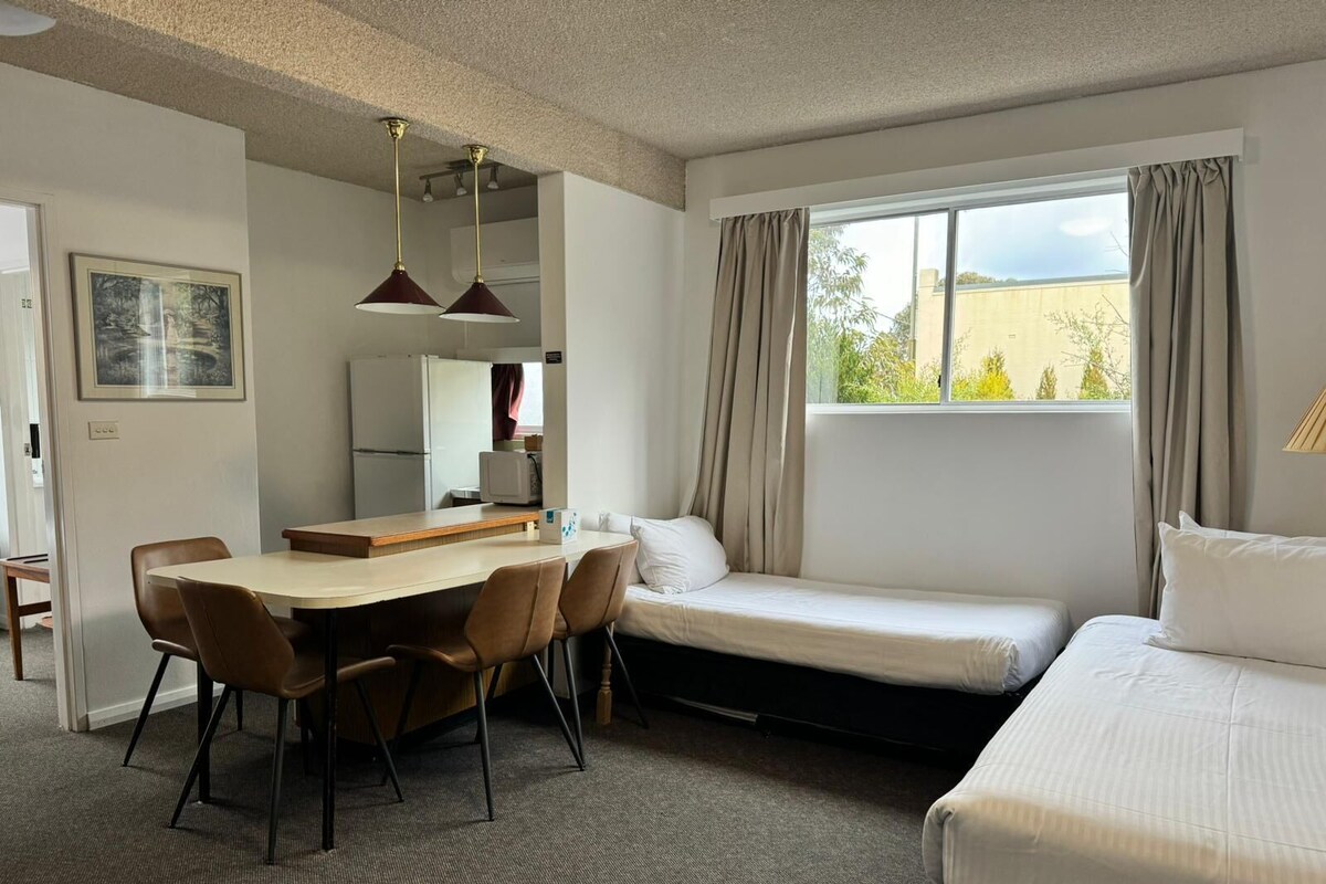 A compact hotel room with a dining area, a bed, and a window with curtains.