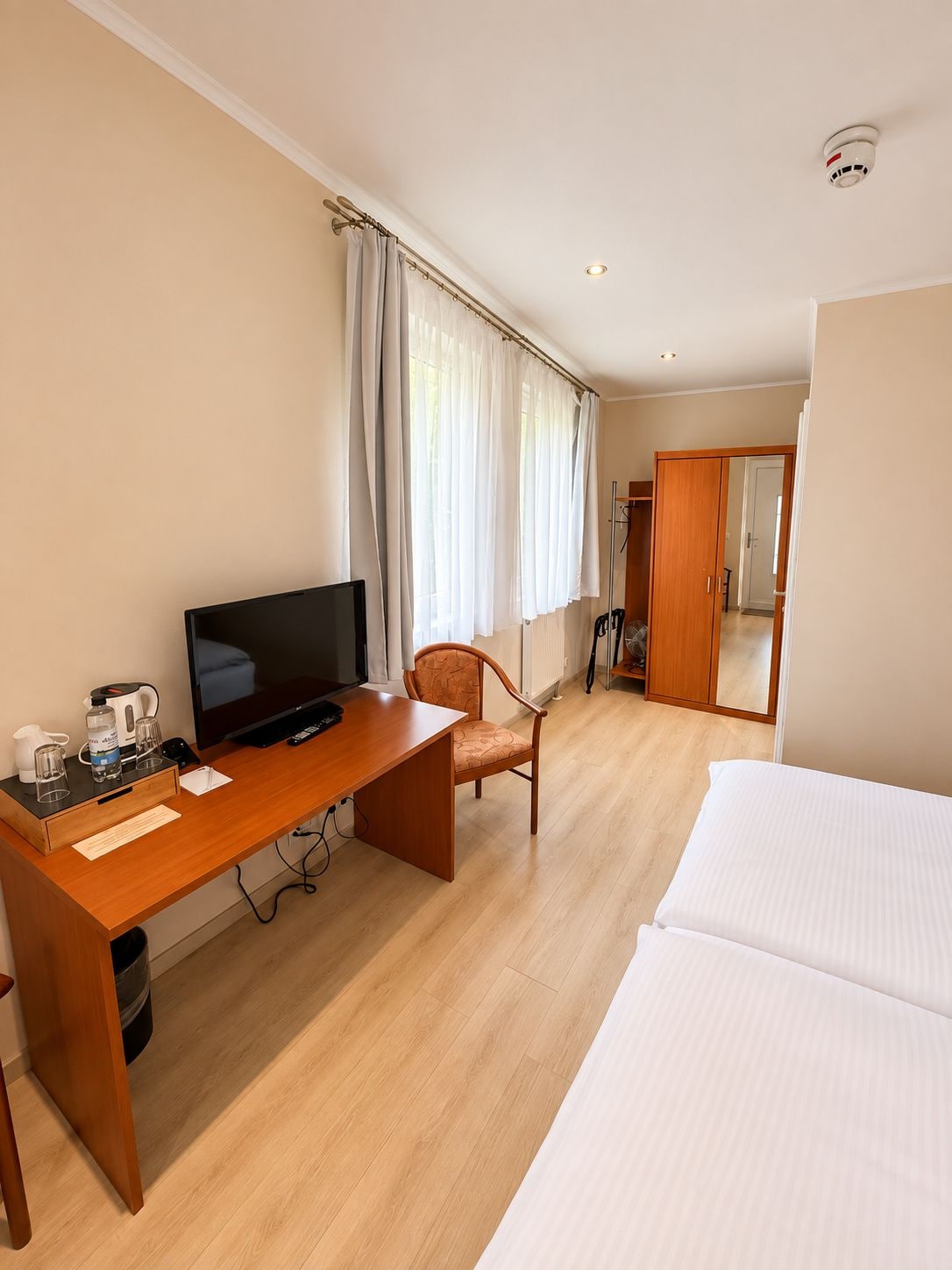 A hotel room with a wooden desk, a television, a chair, a bed, and a bathroom visible through an open door.