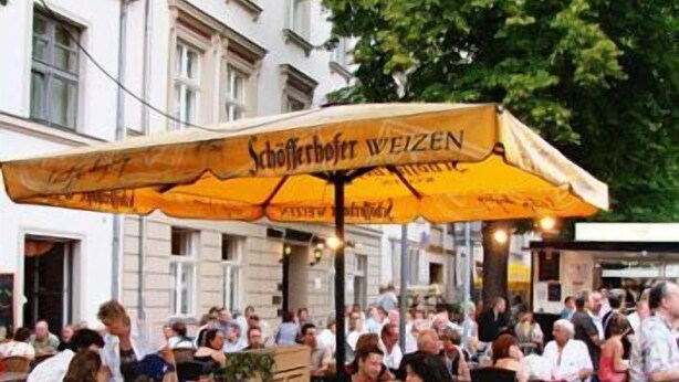 An outdoor dining area with tables and chairs under a large yellow umbrella. - Altstadt Hotel (Potsdam)