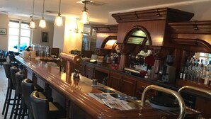A bar area with a long counter, multiple stools, and overhead lighting. - Altstadt Hotel (Potsdam)