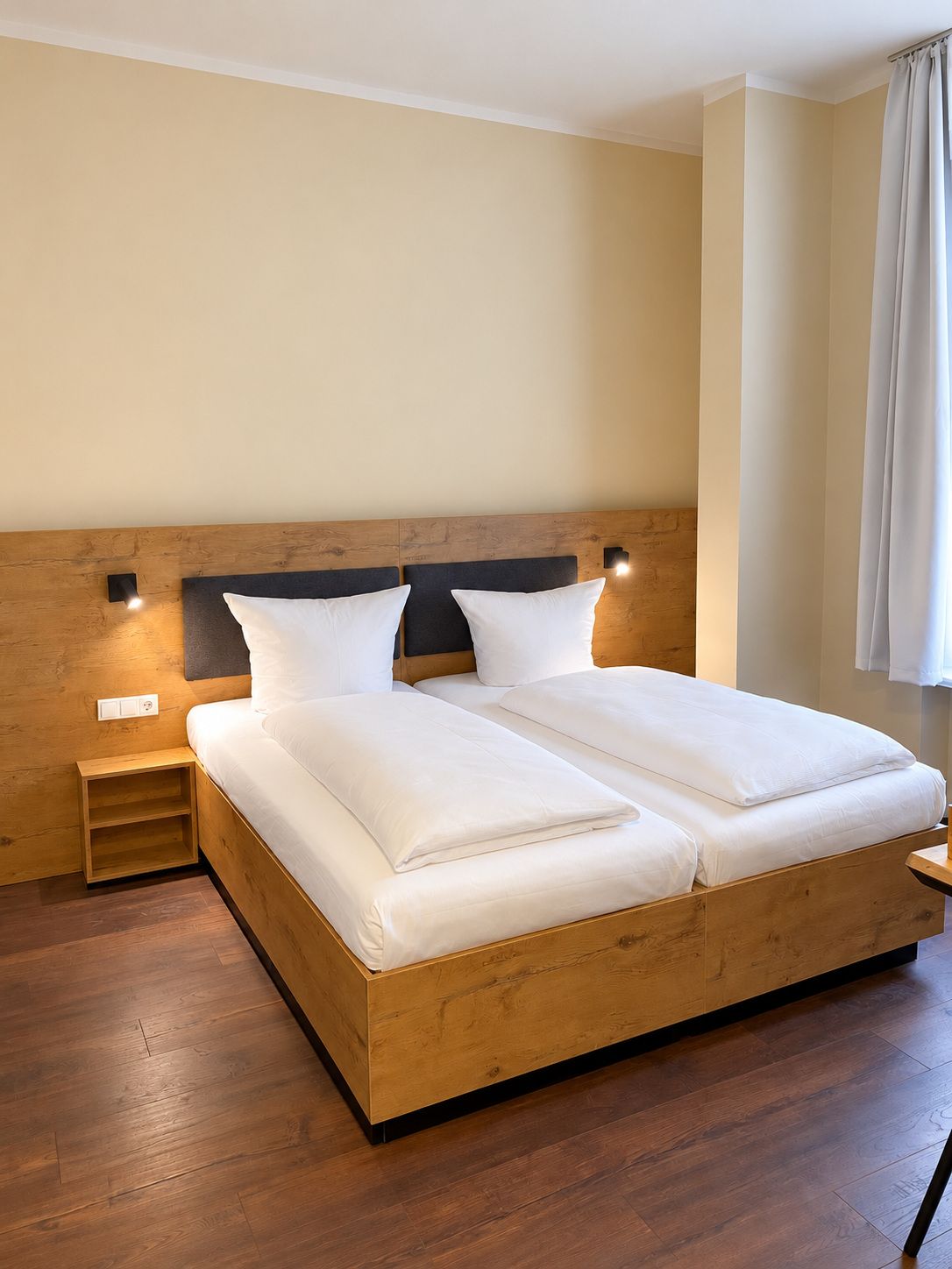 A neatly made bed with a wooden headboard and two bedside tables, one with a lamp.
