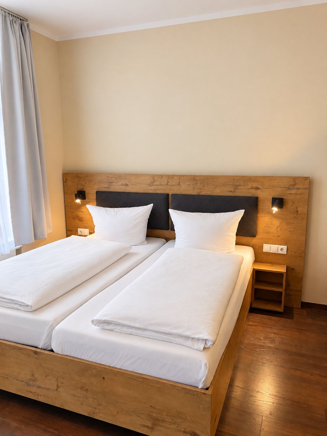 Een tweepersoonsbed met een houten hoofdbord, twee nachtkastjes en een bijzettafeltje.