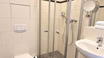 Une salle de bain moderne avec une douche à parois de verre, des toilettes blanches et un lavabo avec un miroir.