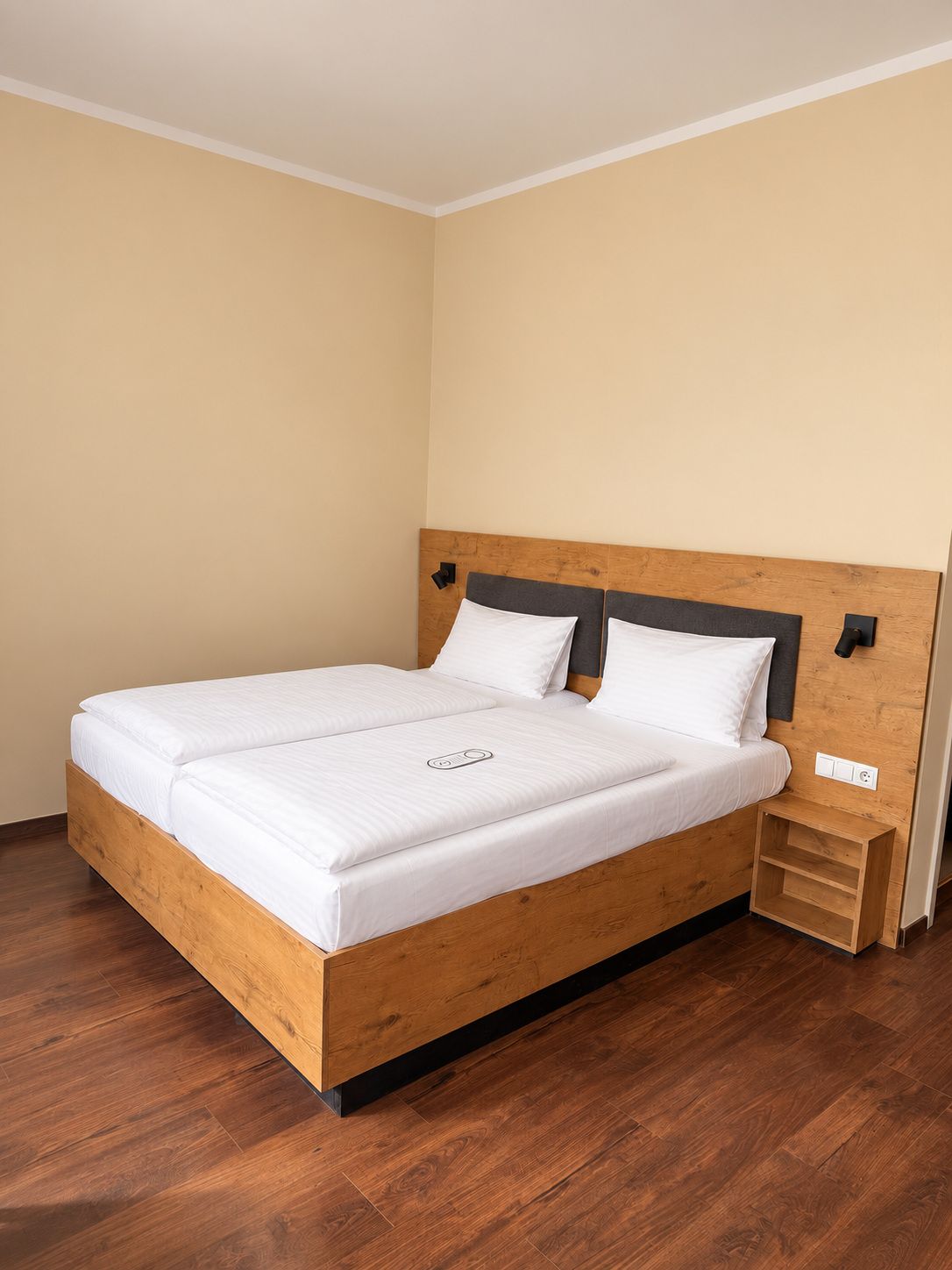 A single-bed room with a wooden headboard, white bedding, and a small bedside table.
