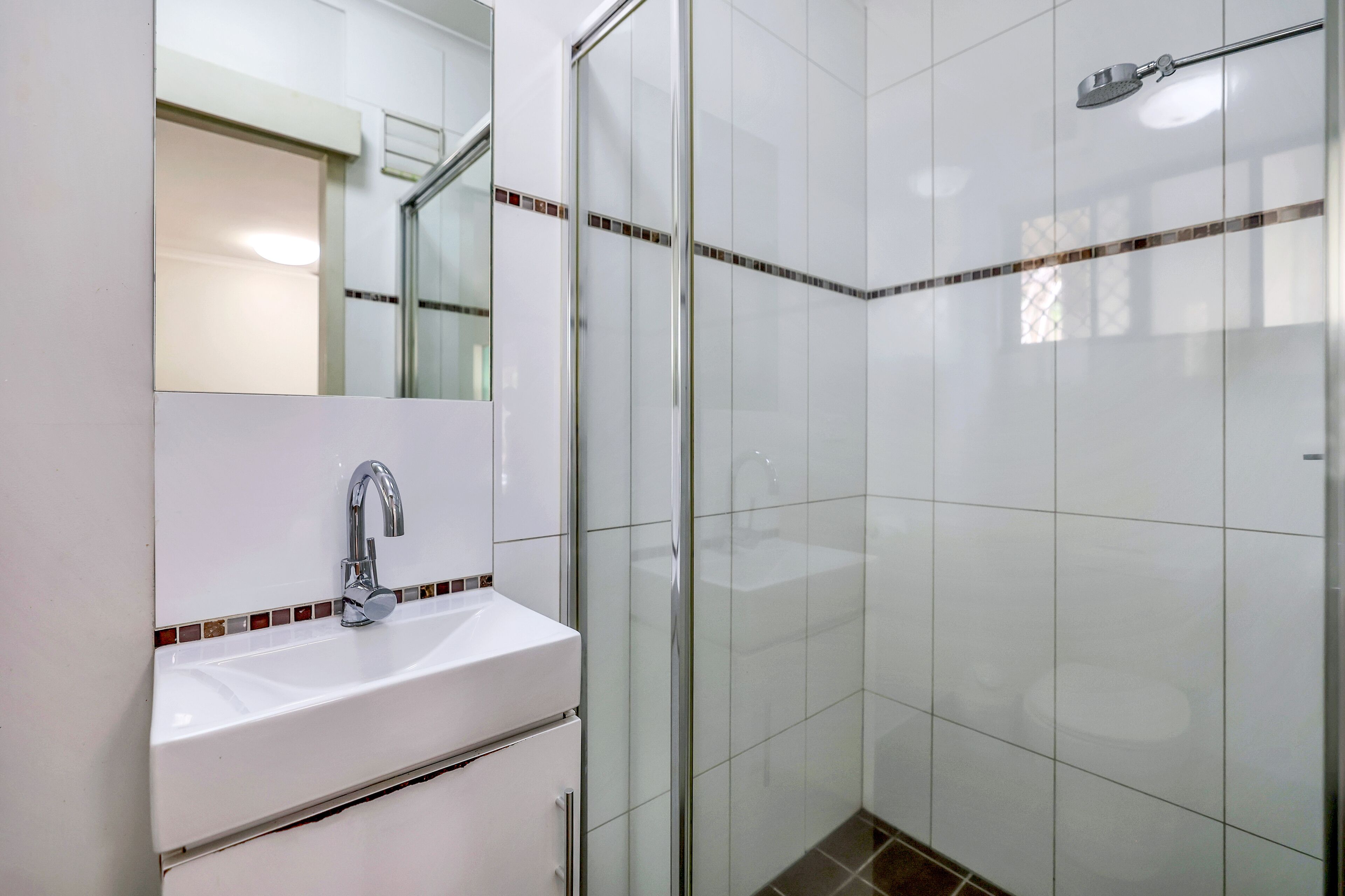 Une salle de bain avec un lavabo blanc, un miroir et une cabine de douche en verre.