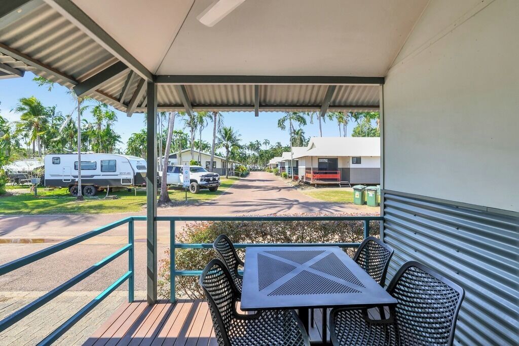 A covered outdoor area with a table and chairs, overlooking a parking lot with RVs and a road.