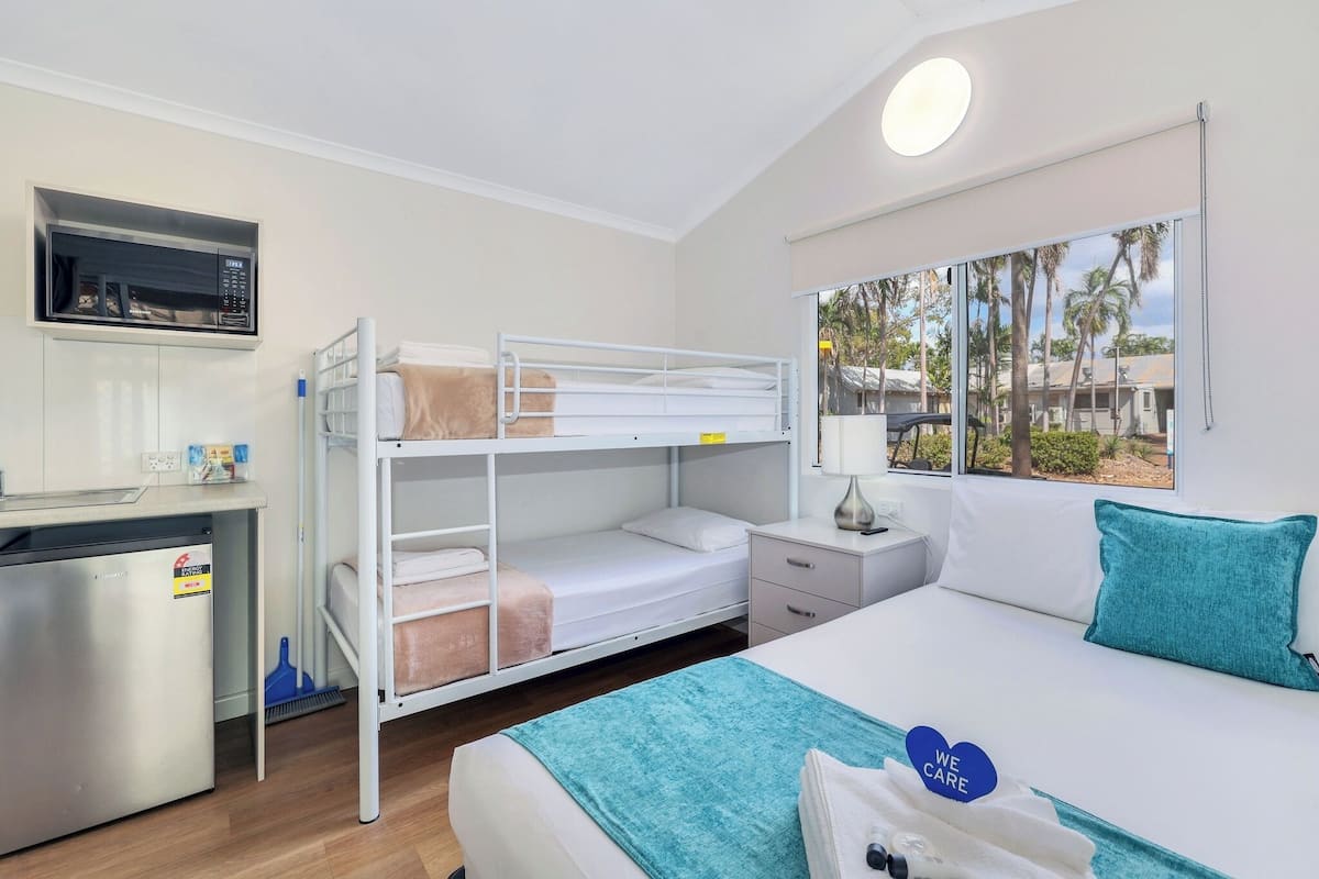 Habitación con literas, escritorio, microondas y ventana con vistas a palmeras.