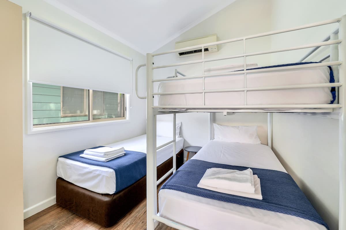 Habitación con literas, una ventana, una mesita pequeña y aire acondicionado instalado en la pared.