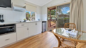 A modern kitchen with white cabinets, a microwave, and a dishwasher. There is a dining area with a glass table and wicker chairs. - Darwin FreeSpirit Resort (Holtze)