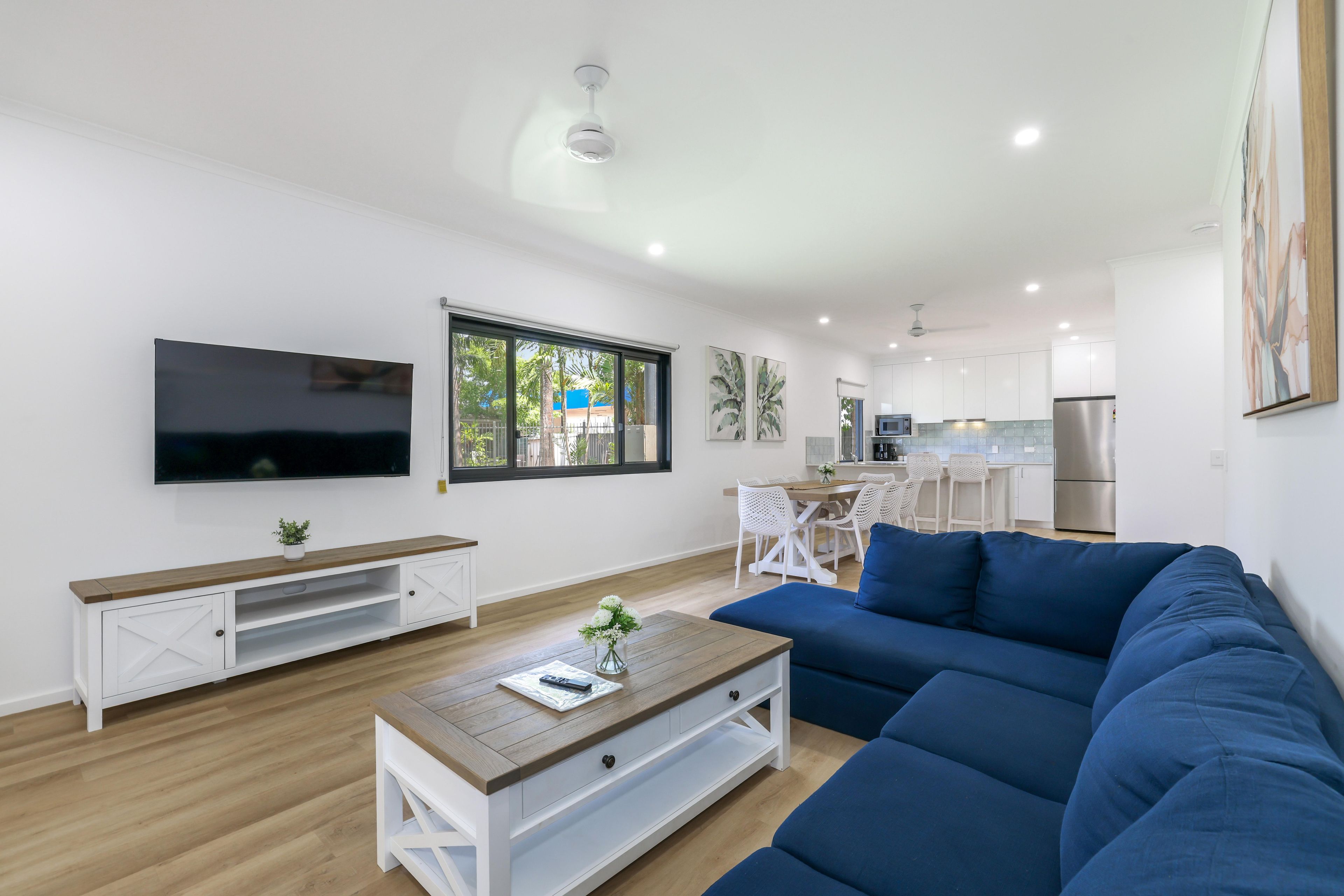 A modern living room with a large blue sofa, a wooden coffee table, and a flat-screen TV mounted on the wall.