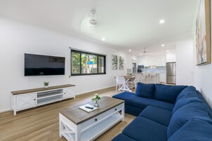 Uma sala de estar moderna com um amplo sofá azul, uma mesa de centro de madeira e uma TV de tela plana na parede.