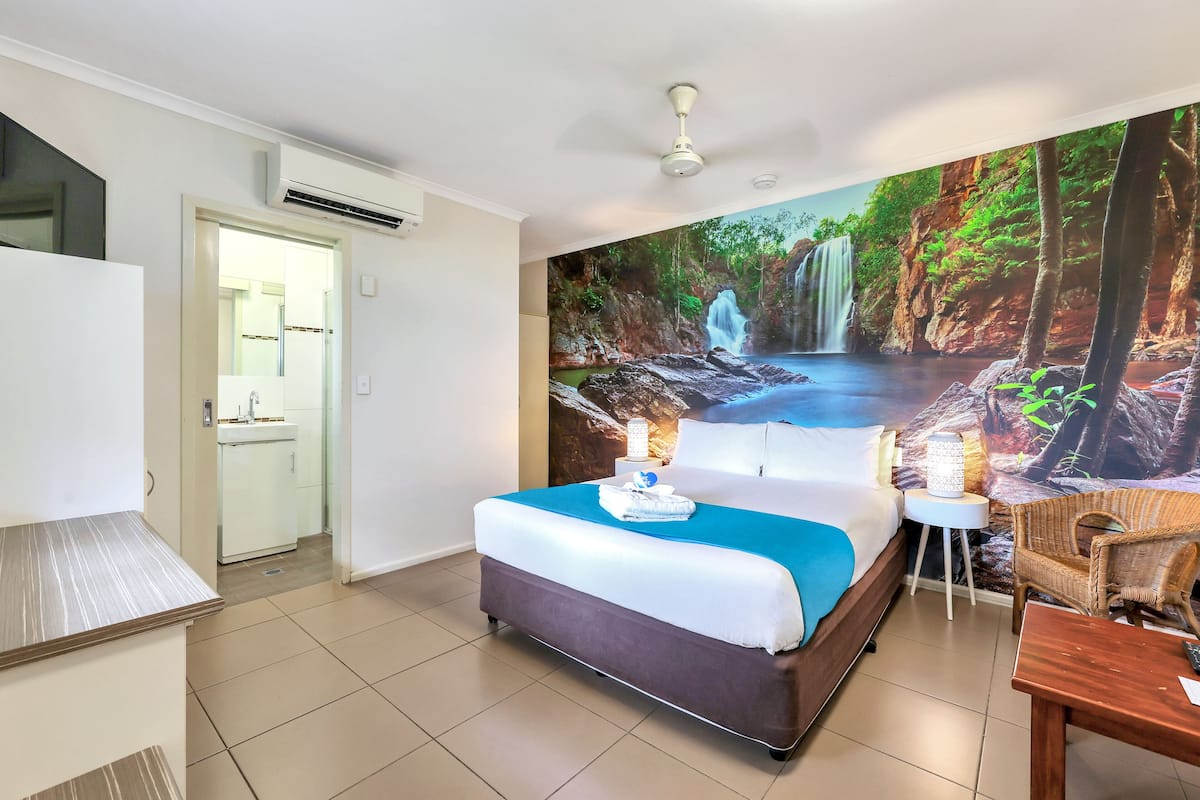 Un dormitorio con una cama grande, una mesita de noche, una silla y un mural en la pared de una cascada.