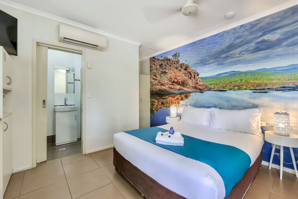Habitación de hotel con cama, baño y un mural de un paisaje.