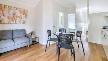 Ein modernes Wohnzimmer mit einem grauen Sofa, einem Esstisch mit schwarzen Stühlen und einem großen abstrakten Gemälde an der Wand.