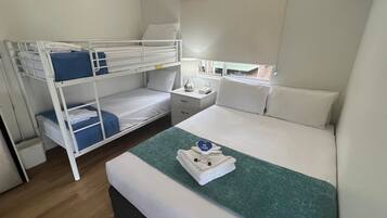 Een hotelkamer met een stapelbed, een eenpersoonsbed, een nachtkastje met een lamp en een raam met uitzicht.