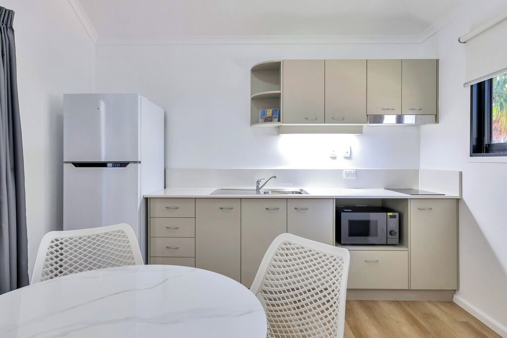 A compact kitchen with a built-in microwave, a sink, and a refrigerator. There are two white chairs and a small table.